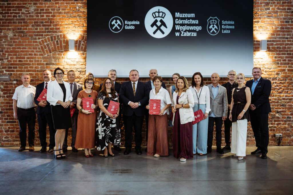 Grupa kobiet i mężczyzn pozujących do wspólnej fotografii na tle logotypów muzeum