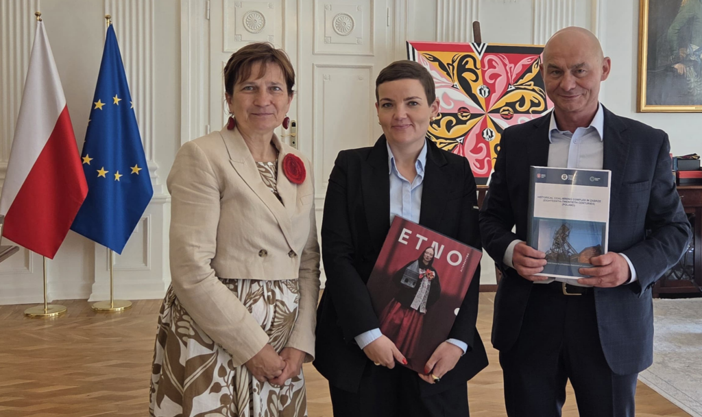 Od lewej stoją: pani Halina Bieda, senator RP, pani Marta Cienkowska, Minister Kultury i Dziedzictwa Narodowego i Bartłomiej Szewczyk, dyrektor Muzeum. Stojący pozują po złożeniu w Ministerstwie wniosku o wpis na listę UNESCO