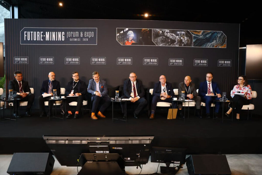 siedmiu prelegentów siedzi pod ścianką promocyjną i bierze udział w dyskusji panelowej podczas forum. Na ściance promocyjnej nazwa Forum Transformacji Śląska