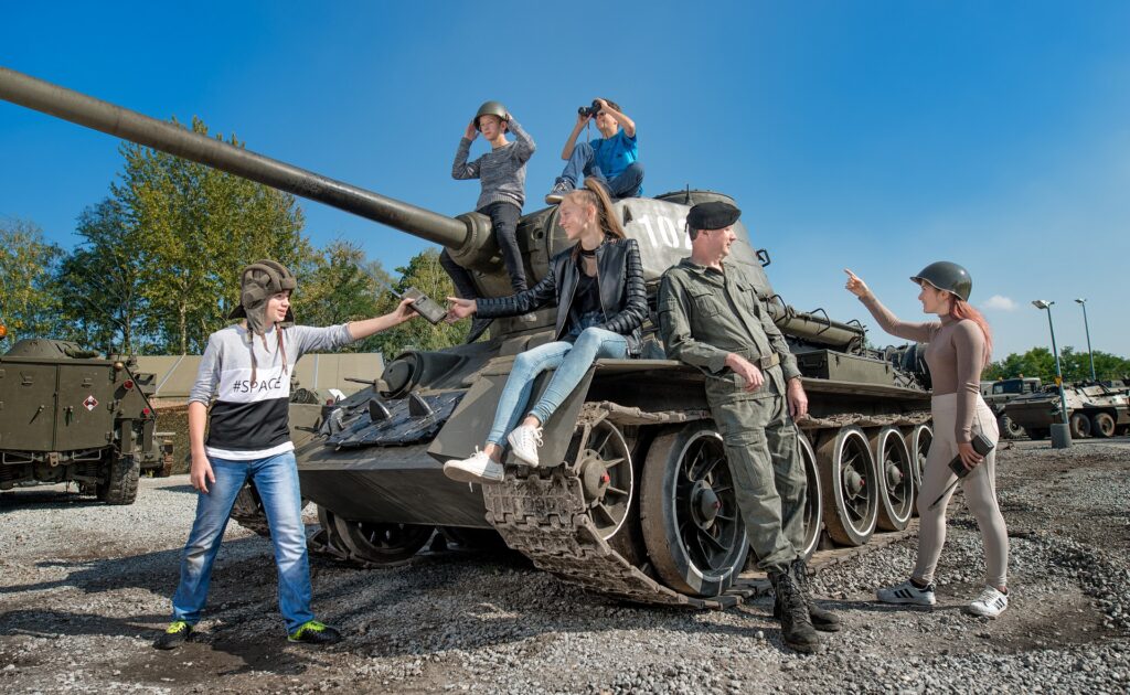 grupa dzieci siedzących na czołgu i żołnierz, park techniki wojskowej