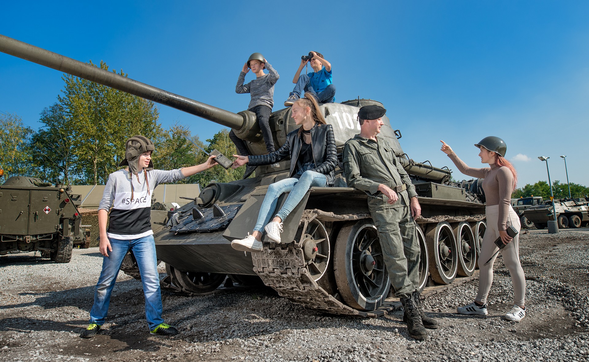 grupa dzieci siedzących na czołgu i żołnierz, park techniki wojskowej